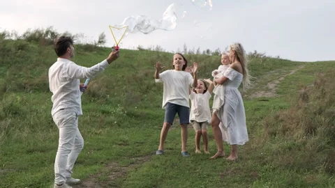 The father blows soap bubbles and the family catches them and rejoices. Stock Footage 283762432