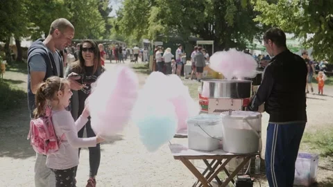 Father buys candy floss for little girl from stall at festival fairground Stock Footage 193370208