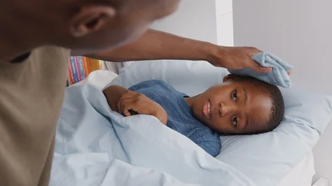 Father Caring For Sick Son Ill In Bed Taking Temperature With Thermometer Stock Footage