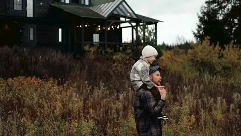 Father carries child on shoulders, with a rustic house in the background Stock Footage 319962247