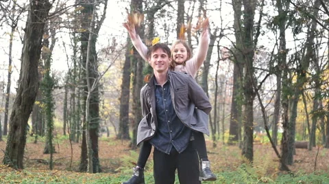 Father carrying daughter on back and she is throwing leaves in the air Stock Footage 59553907