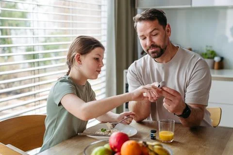 Father checking blood sugar level of diabetic teenage daughter using glucose  Stock Photos