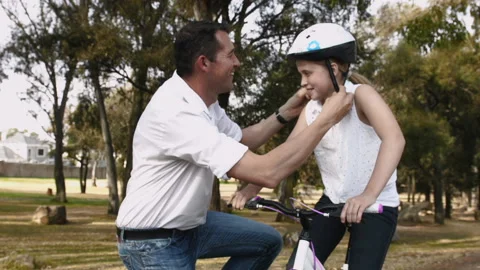 Father clipping helmet on daughters head before she starts to ride her bike. Ste Stockbeeldmateriaal 199630853