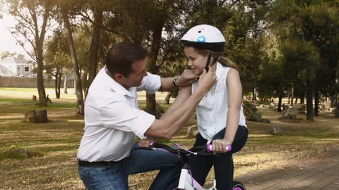 Father clipping helmet on daughters head before she starts to ride her bike. Ste Vidéo 199630862