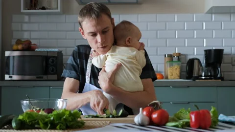 Father cooking salad while holding baby in hands Stock Footage 225064514