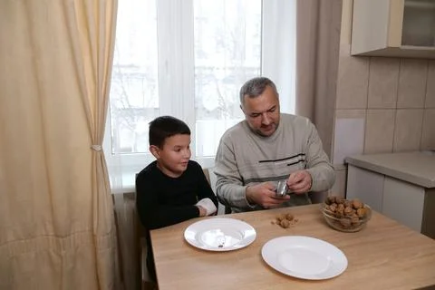 Father cracks a walnut with a nutcracker while the boy sits next to him watch Stock Photos