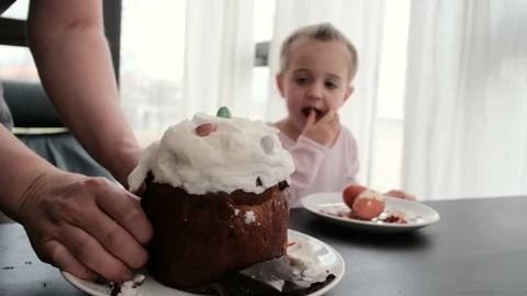 Father cuts Easter cake to treat girl at table in light room Stock Footage 154395658