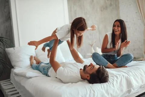 Father doing exercises with kid on bed while mom watching Stock Photos