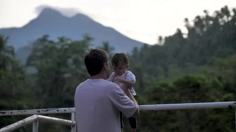 A father, dressed in summer clothes, throws up his handsome little son, who is Stock Footage 181276359