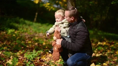 Father embraces his  capricious son in autumn park. Blond hair kid boy with tedd Stock Footage 218606810