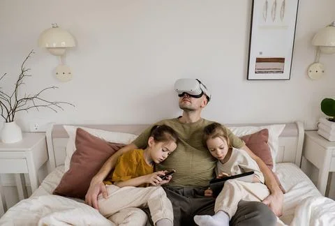 A father is enjoying virtual reality while his two daughters sit beside him,  写真素材