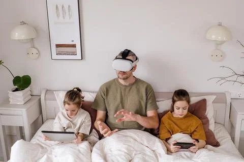 A father is experiencing virtual reality while his two daughters sit beside h Stock Photos
