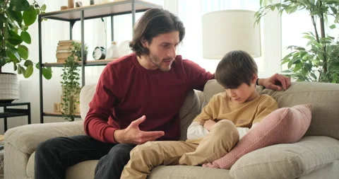 Father explaining to his sad son sitting on sofa Stock Footage 145235676