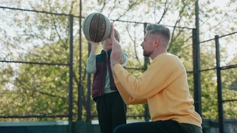 Father explaining to son how to hold and throw a basketball ball on a sunny day Vídeo Stock 166837535