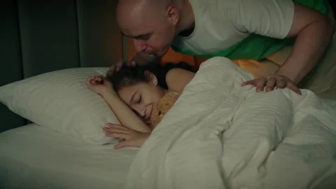 Father gently covers his sleeping daughter with a blanket as she cuddles her Stock Footage 313746665