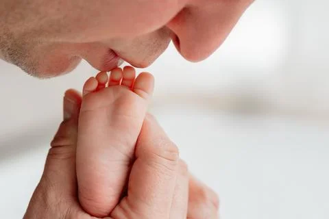 Father gently kissing tiny newborn baby feet. Stock Photos