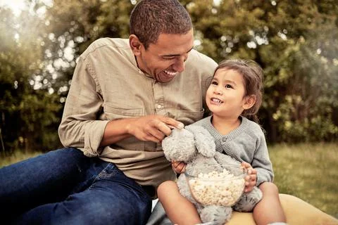Father, girl and popcorn eating of a happy child and parent outdoor laughing Stock Photos