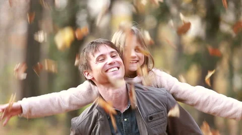 Father gives daughter piggyback ride while she throws leaves in the air Stock Footage 59554402