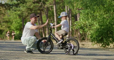Father gives son high five during bicycle practice in forest park Stockbeeldmateriaal 316760745