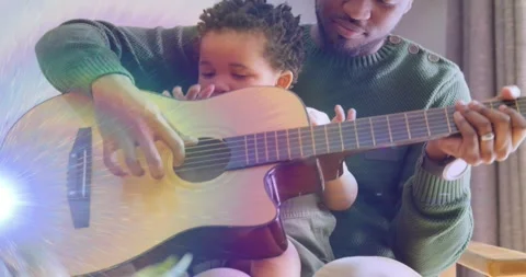 Father guiding baby's hands while baby reaching and strumming guitar at sound Stock Footage 330258493