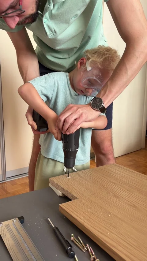 Father guiding young child using cordless drill for a DIY project Stock Footage 341396581
