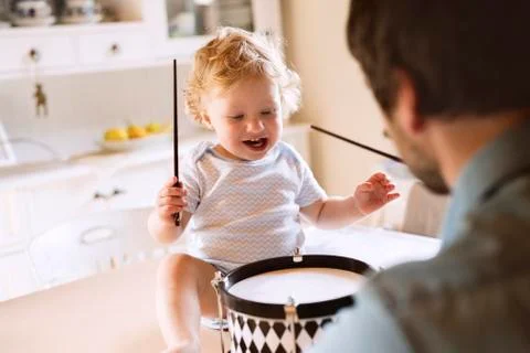 Father with happy little boy sitting on kitchen table playing drum Stock Photos