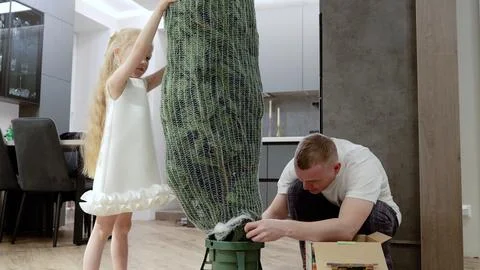 Father helping daughter assembling artificial christmas tree, decorating living Stock Photos