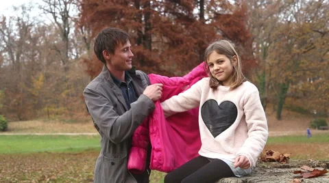 Father helping daughter put on jacket in the park Stock Footage 59553961