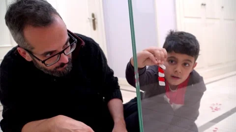 Father helping his son place Christmas decoration on glass door 스톡 동영상 345253190