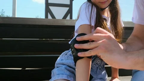 Father helping kid to put on protective wrist guards for roller skating outdoors Stock Footage 280859967