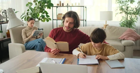 Father helping son doing homework from textbook and mother using digital tablet Stock Footage 145231654