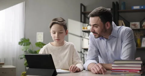 Father helping son doing homework, study online sitting at home desk using Stock Footage 272989948