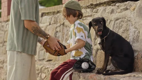 Father Helping Son Fitting Baseball Glove with Dog Sitting Nearby Stock Footage 340259215