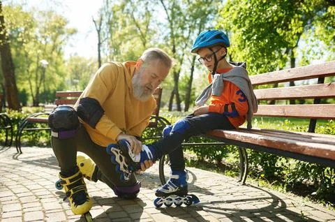 Father helping son to put on roller skates in urban park Stock Photos
