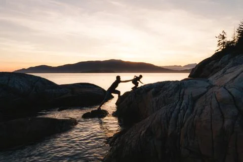 Father helping son on rocks while sunset Foto stock