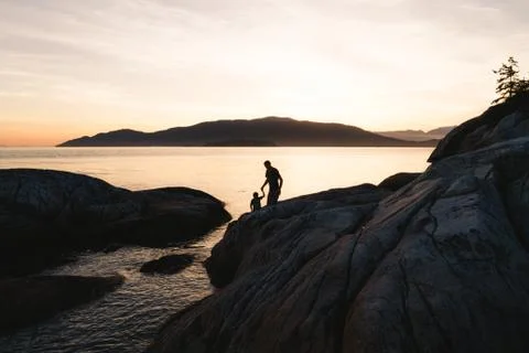 Father helping son on rocks while sunset Stock Photos