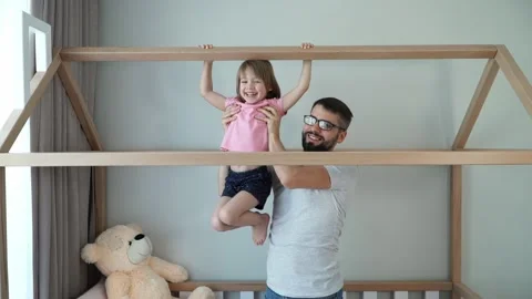 Father helps girl pull up on horizontal bar at home, play active games and laugh Stock Footage 146954686