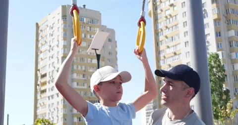 Father helps son exercise playground rings. Child trains with focus while dad Vidéo 315533663