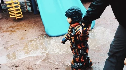 Father hold hand little boy on children playground. Family. Raining weather Stock Footage