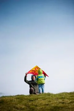 Father holding kite while crouching with son on field against clear sky Stock Photos