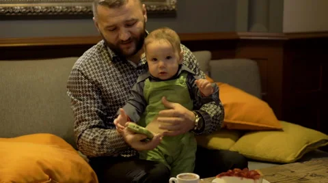 Father holding son and using phone in restaurant Stock Footage 60662420
