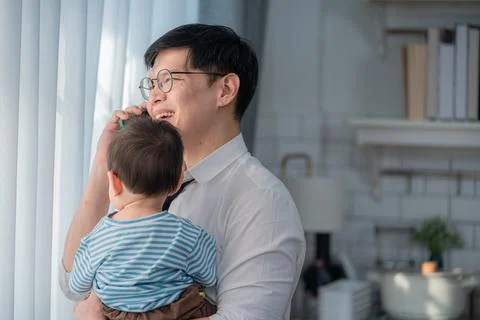 Father holds child while talking on the phone in a bright, modern living ro.. Stock Photos