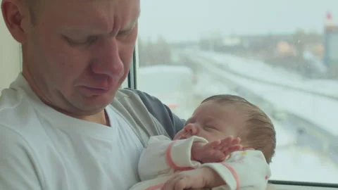 Father holds his tiny, sleepy newborn baby in his arms while standing by window Video stock 316155191