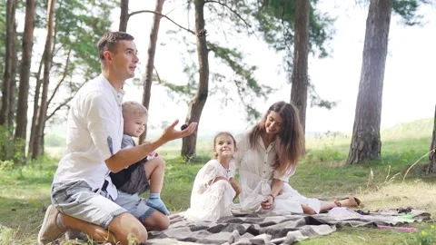 Father juggles with cones from a pine tree. Family picnic with two kids. Slowmo Stock Footage 205479335