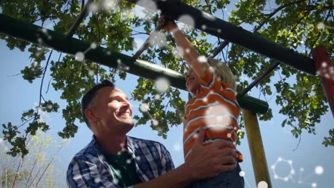 Father kneeling under green monkey bars, lifting boy and supporting swinging for Stock Footage 318238995