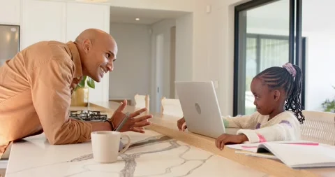 Father leaning forward on marble island guiding daughter studying at kitchen Stock Footage 337705079
