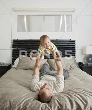 Father Lifting Son On Bed In Bedroom