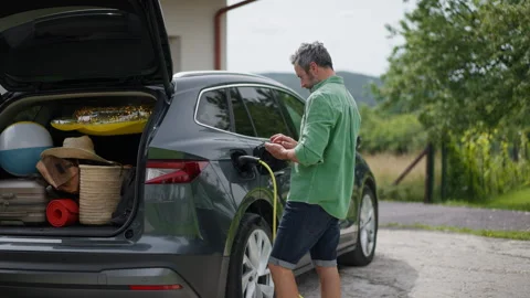 Father loading luggage into trunk of electric car with charger in charging port Video stock 282050119
