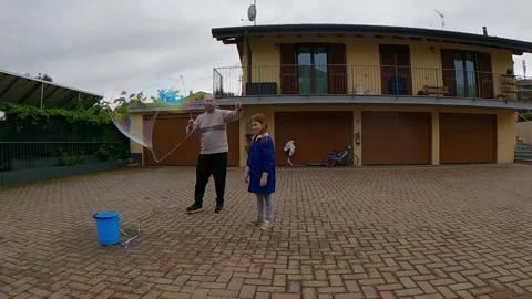 Father making giant soap bubble with daughter in backyard, slow motion Видео 279423712