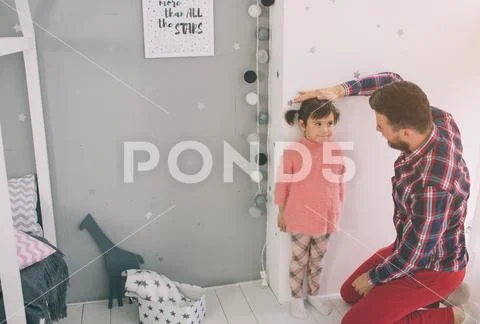 Father is measuring his baby height on the wall. Cute little daughter and her Stock Photos